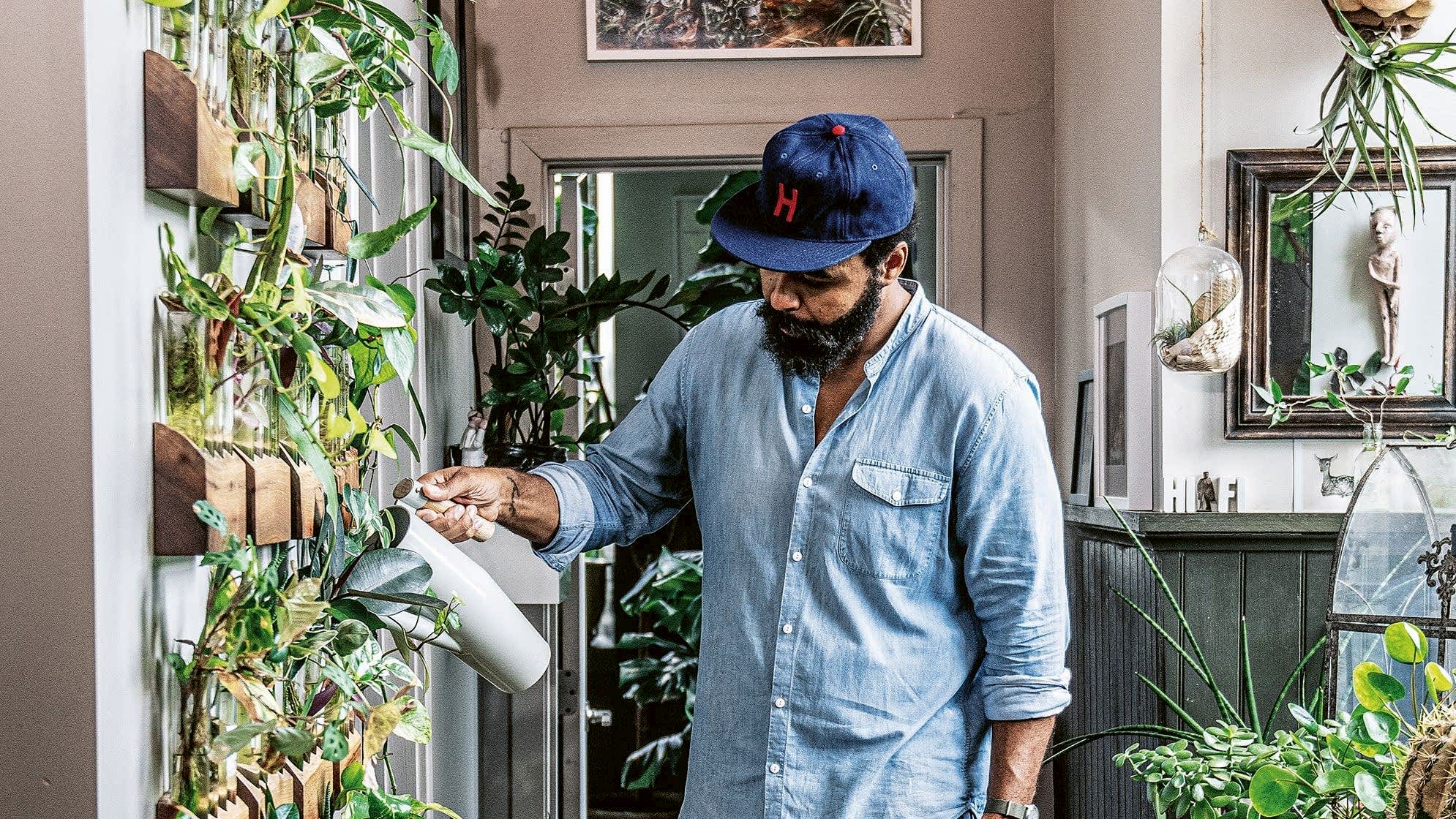 Hilton Carter tending watering a living wall of plants in his apartment hallway